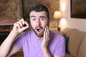 A man holds his missing tooth in one hand while clutching his jaw in pain, clearly in need of a dental implant.