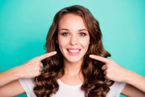 Woman smiling and pointing at her straight, white teeth after receiving All-on-4 implants